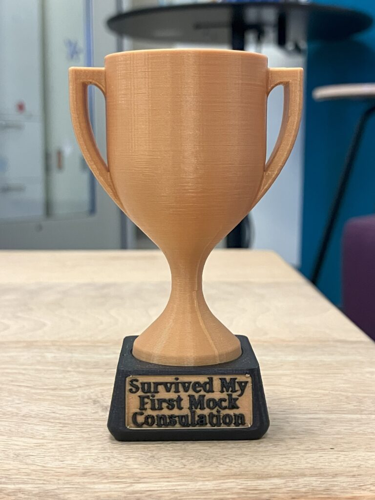 3D printed miniature trophy reading "I Survived My First Mock Consultation"